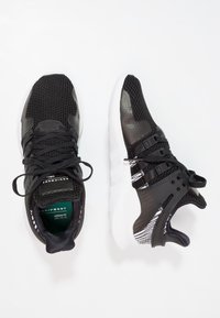 Svarta träningsskor med överdel av mesh och syntetmaterial, vit sula, texturerade detaljer och svarta snören. Har en märkesinläggssula och unika designelement.