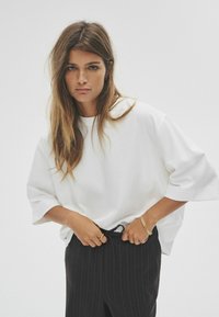 Biała, oversize koszulka z krótkim rękawem w połączeniu z czarnymi spodniami w paski. Prosty design, miękka tekstura i luźny krój.