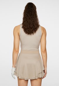 Top atletico beige con un design a fantasia e una gonna corta svasata. Presenta una vita aderente e un orlo a strati. Guanto bianco sulla mano sinistra.