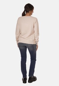 Pullover a maglia color beige chiaro con maniche lunghe, orlo a coste e dettagli sulla cucitura posteriore. Abbinato a jeans blu scuro e scarpe con piattaforma nere.