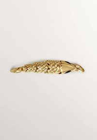 Accesorio en tono dorado con forma de pez, que presenta un cuerpo texturizado, aleta suave y ojos de acento negro. Incluye un lazo para su sujeción.