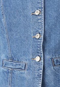 Lys blå denimjakke med fire sølvsnapknapper, vertikale sømmer og to små frontlommer med en lett tekstur.