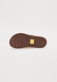 Talpa din cauciuc maro cu un design texturat prezentând modele de frunze. Include un eticheta rectangulară galbenă cu numele brandului în centru.