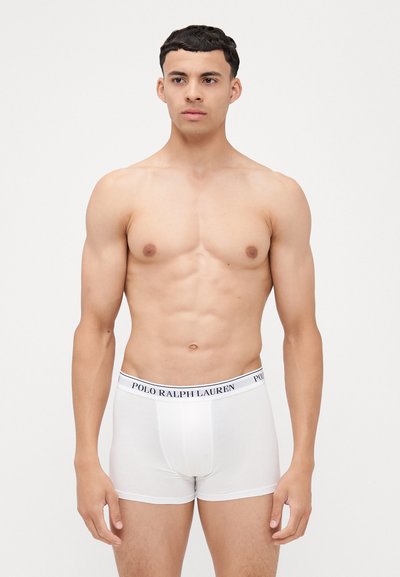 Beli bokserice z mornarsko modrim pasom, na katerem je napis "POLO RALPH LAUREN". Tkanina izgleda gladko in je oprijeta okoli pasu in stegen.