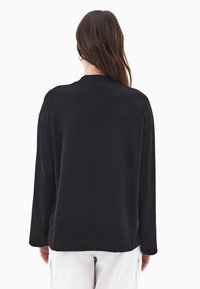 Czarna koszula z długim rękawem, charakteryzująca się okrągłym dekoltem, luźnym krojem i gładką fakturą. Tył jest gładki, bez widocznych logo ani wzorów.