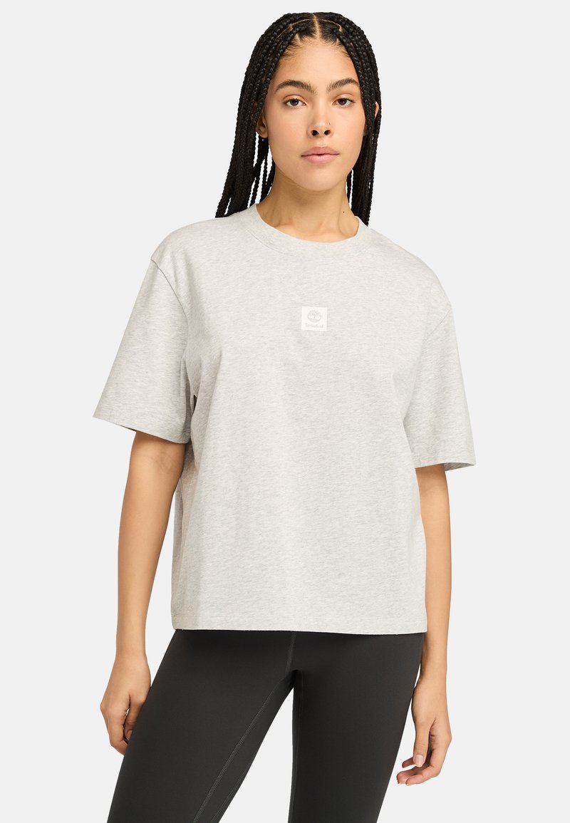 Šedé tričko s krátkým rukávem z bavlny, s vyšitým čtvercovým logem Timberland uprostřed, volného střihu a kulatým výstřihem.