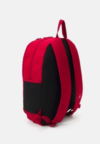 Sac à dos rouge et noir au design épuré, avec un extérieur en tissu lisse, des bretelles réglables et une poignée de transport supérieure.