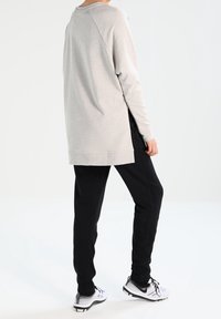 Haut gris clair à manches longues avec une coupe décontractée, un ourlet arrondi et des poignets côtelés, associé à un pantalon noir fuselé et des chaussures de sport blanches.