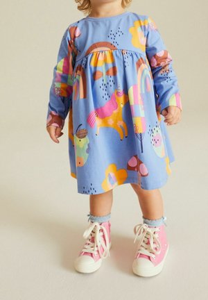 Vestido azul de manga larga con estampados coloridos de animales y flores, cintura fruncida y detalles en rosa. Combinado con zapatillas altas rosas.