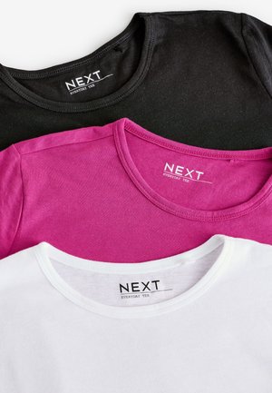 Trois t-shirts étalés à plat : noir, fuchsia et blanc. Chacun a un col rond et l'étiquette « NEXT EVERYDAY TEE » en texte noir.