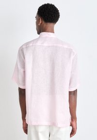 Lichtroze linnen shirt met een ontspannen pasvorm, korte mouwen en een zachte textuur. Bevat een kleine kraag en contrasterende afwerking.