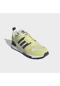 Lime green athletic shoe with mesh and suede materials, featuring three navy stripes, a rounded toe, cushioned sole, and dark outsole.