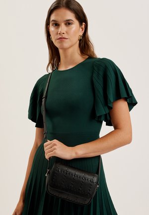 Zwarte leren crossbodytas met een doorgestikt patroon, voorzien van een ritssluiting en verstelbare riem. Rondvormig, gladde textuur, minimalistisch design.