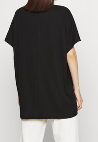 Černý oversized top s krátkými rukávy, žebrovanou strukturou a zaobleným lemem. Lehce materiál, volný střih a minimalistický design.