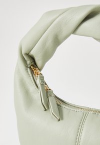 Green faux leather handbag with a twisted handle, gold zipper hardware, and a textured surface. Side zipper detailing visible.