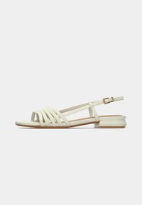 Sandales plates en blanc cassé, avec plusieurs designs de lanières, bout ouvert, bride à la cheville avec boucle, et talon carré bloc pour une stabilité optimale.