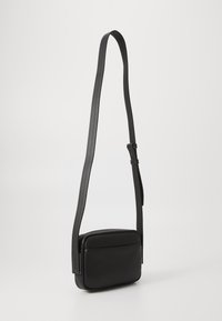 Black leather crossbody bag with a flat rectangular shape, adjustable strap, and minimalistic design. Features a smooth texture and no visible hardware.
