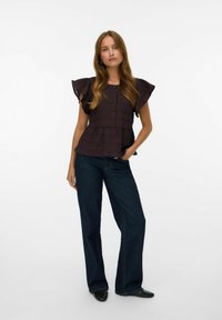 Un top marrone scuro a coste con maniche corte arricciate, chiusura con bottoni sul davanti e vita a peplum, abbinato a jeans in denim scuro a zampa.