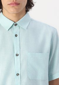Himmelblaues Kurzarmhemd aus strukturiertem Stoff, mit Knopfleiste, Kragen und einer Brusttasche.