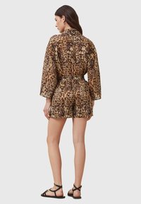 Animal print romper in brown and tan with a loose fit, long sleeves, elastic waist, and shorts. Complemented by black strappy sandals.