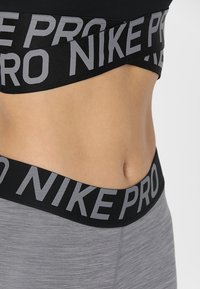 Nike Pro sports bra with a black band featuring gray lettering. Gray textured leggings with a similar black waistband.