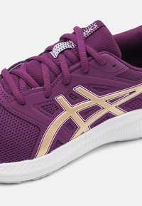 Fioletowy but sportowy z siateczkowej tkaniny i złotymi akcentami. Posiada teksturowaną cholewkę, sznurówki oraz białą gumową podeszwę dla lepszej przyczepności.