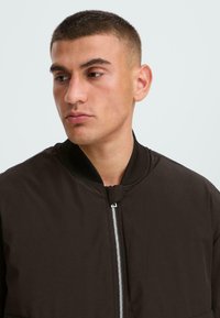 Black bomber jacket with a ribbed collar, zip closure, and a smooth texture. Close-up view of the upper body and neckline.