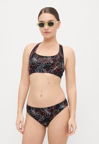 Black bikini set featuring floral patterns in red, blue, and yellow. The sports top has wide straps and a logo; bottoms are low-rise with a seamless design.
