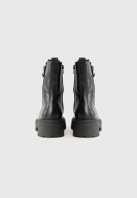 Botas de cuero negras hasta el tobillo con suela de goma gruesa, cremalleras laterales y textura suave, que ofrecen una silueta moderna y elegante.