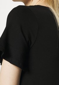 Czarny krótki top z rękawami, wykonany z miękkiej bawełny, z subtelnym falbanym wzorem na rękawach i gładkim, dopasowanym dekoltem.