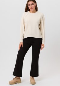 Crèmewitte sweatshirt met geribbelde textuur aan één zijde, voorzien van een ronde halslijn. Gecombineerd met zwarte uitlopende broek en beige schoenen.