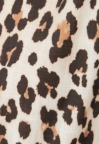 Tissu imprimé léopard présentant des taches irrégulières brun foncé et beige clair sur un fond crème, avec une apparence douce et texturée.