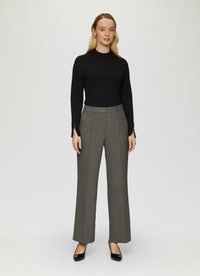 Un haut en maille noir à manches longues associé à un pantalon large gris taille haute. Le pantalon présente un subtil motif en chevrons et des plis sur le devant.