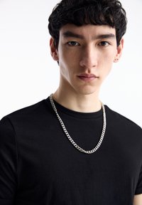Tricou negru cu mânecă scurtă, cu gât rotund, având un colier strălucitor din lănțișor argintiu cu inele împletite în jurul gâtului.