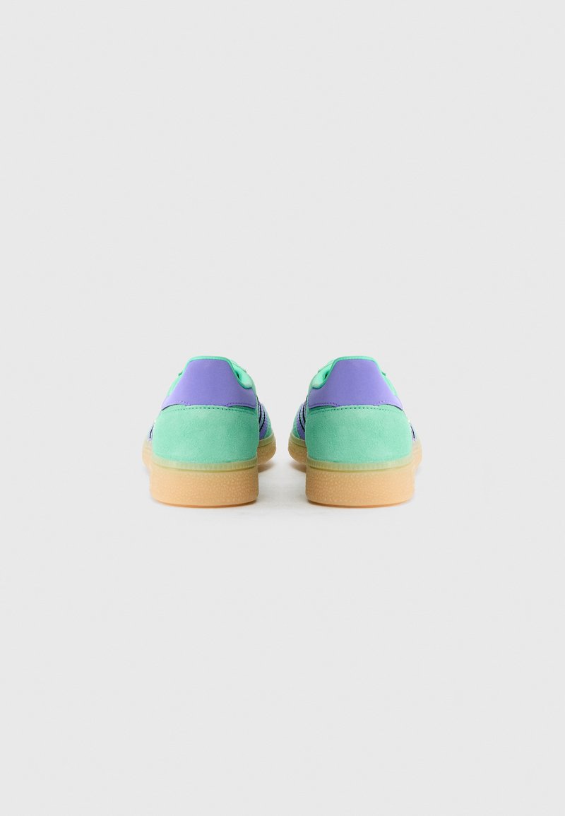 Sneakers with a purple and green suede upper, featuring a textured gum rubber sole and contrasting laces. Rounded toe design.