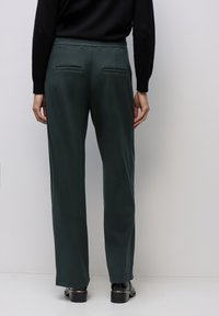 Mörkgröna, vida byxor i slätt tyg med elastisk midja och två bakfickor. Plana sömmar och inga synliga knäppningar.