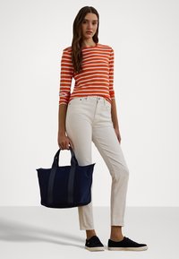 Raitapaitainen pitkähihainen paita oranssin ja valkoisen sävyissä, valkoiset slim fit -farkut, tummansininen olkalaukku harmailla kahvoilla ja mustat lenkkarit. Liukkaat pinnat kauttaaltaan.