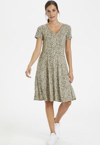 Short green floral dress with a V-neck, short sleeves, and a flared skirt, paired with white sneakers. Pattern features small white flowers.
