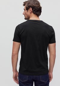 Sort t-shirt med korte ærmer og rund halsudskæring; blød tekstur og tætsiddende design. Båret med blå jeans, set fra ryggen.