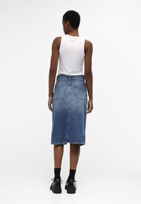 Jupe midi en denim bleu clair avec une taille ajustée, deux poches arrière et une longueur juste en dessous du genou. Assortie à des chaussures et des chaussettes noires.