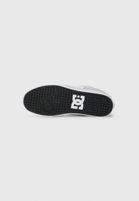 Suela de zapatilla gris con suela negra, mediopie blanco y logo blanco de DC Shoes en el centro de la suela.