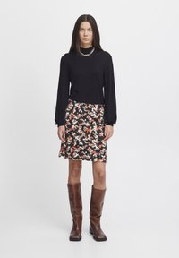 Un haut à manches longues noir associé à une jupe fleurie de longueur genou aux couleurs rouge, blanc et vert, complété par des bottes marron jusqu'au genou.