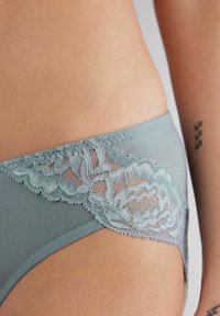 Lichtblauwe katoenen slipjes met fijne kantdetails langs de tailleband, met een golvende rand en een zachte, gladde textuur.