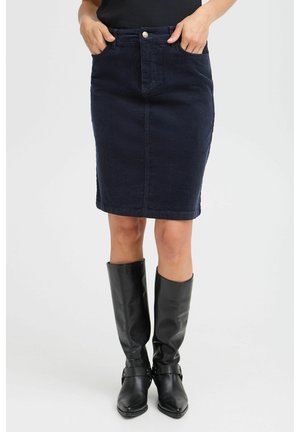 Jupe en denim bleu marine, à coupe droite et mi-longue, avec des poches avant et une fermeture à boutons sur le devant. Portée avec des bottes noires jusqu'aux genoux.