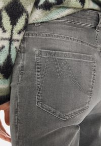 Grijze denim jeans met een achterzak met opvallende stikdetails, gecombineerd met een textuurrijke, multi-kleurige gebreide trui.