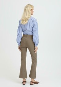 Blusa de rayas azul y blanca con mangas abullonadas, combinada con pantalones de campana verdes oliva. Zapatos marrones tipo slip-on completan el conjunto.