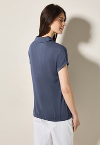 Námořnická modrá polokošile s ohrnutými rukávy, s hladkým povrchem a elastickým lemem v pase. Jednoduchý design s klasickým límečkem.