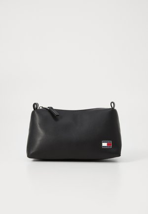 Black cosmetic bag with a smooth texture, rounded shape, zipper closure, and a small logo patch featuring red, white, and blue accents.