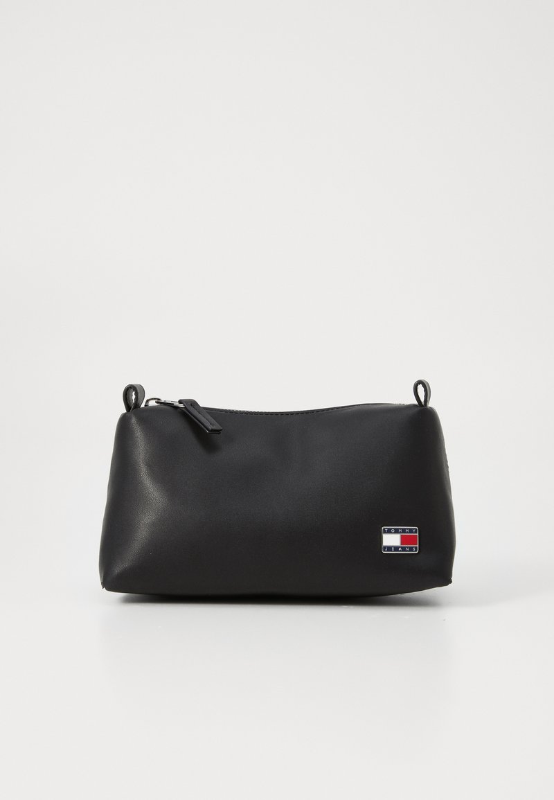 Neceser negro con una textura suave, forma redondeada, cierre de cremallera y un pequeño parche con logo que presenta acentos en rojo, blanco y azul.
