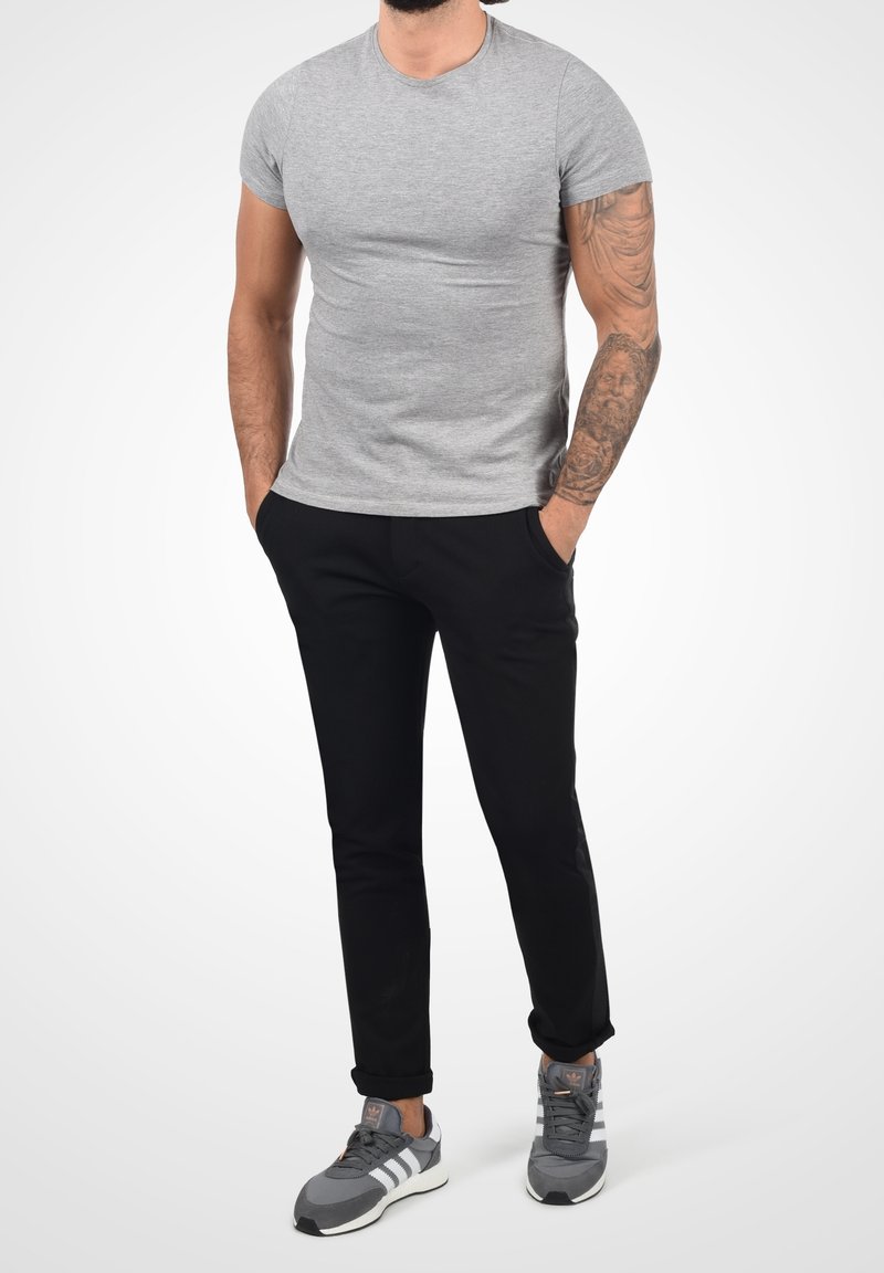 Grijze katoenen t-shirt, korte mouwen, ronde hals; gecombineerd met zwarte broek en grijze sneakers met witte accenten.